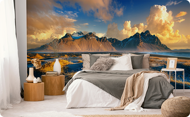 Mountain landscape wallpaper mural with golden clouds and blue waterways behind a bed with gray bedding